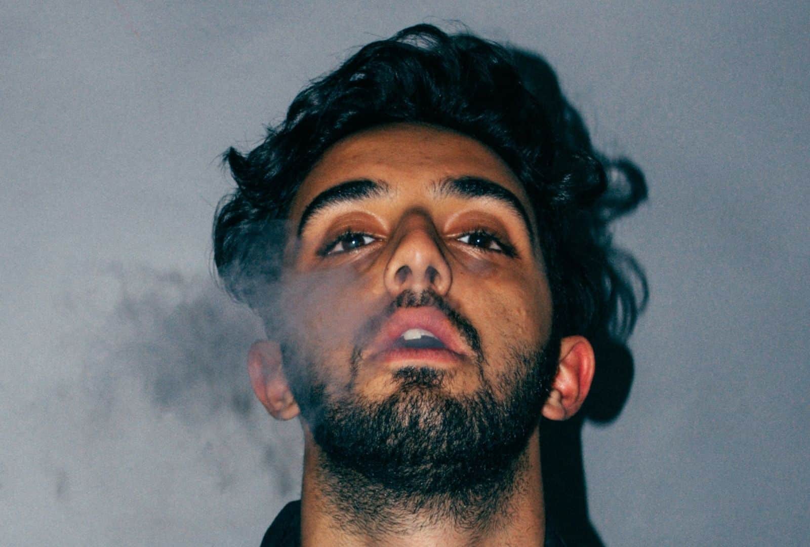 צעיר מביט למעלה בעוד עשן סביב פניו, מבט המשקף מצוקה ובלבול – בהקשר של ליווי הורים לילדים מכורים.