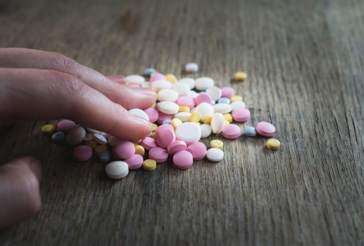 יד נוגעת בערימת כדורי משככי כאבים צבעוניים על עץ, סמל להתמכרות – טיפול רגשי בהרצליה עם דברת קשתי.