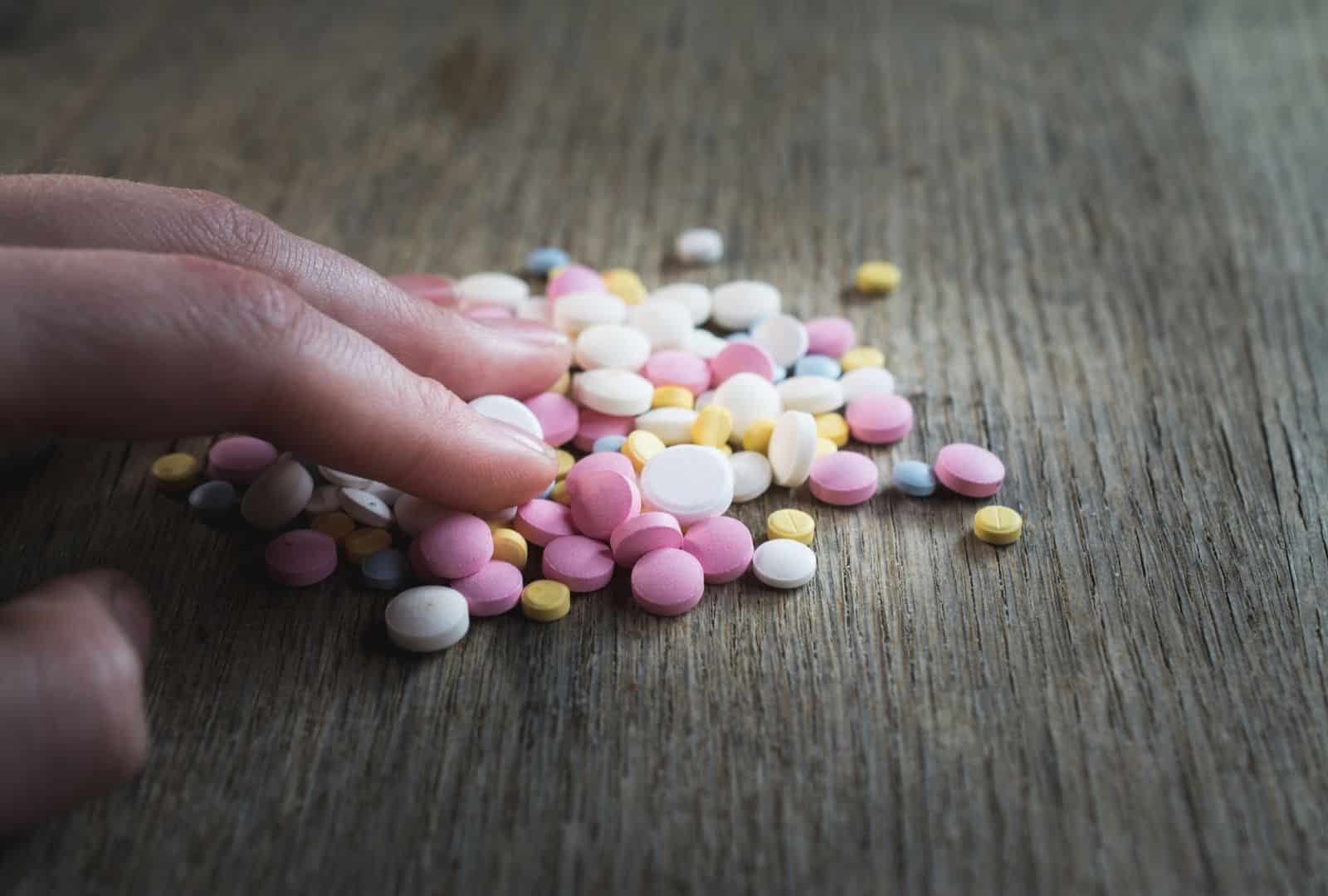 יד נוגעת בערימת כדורי משככי כאבים צבעוניים על עץ, סמל להתמכרות – טיפול רגשי בהרצליה עם דברת קשתי.