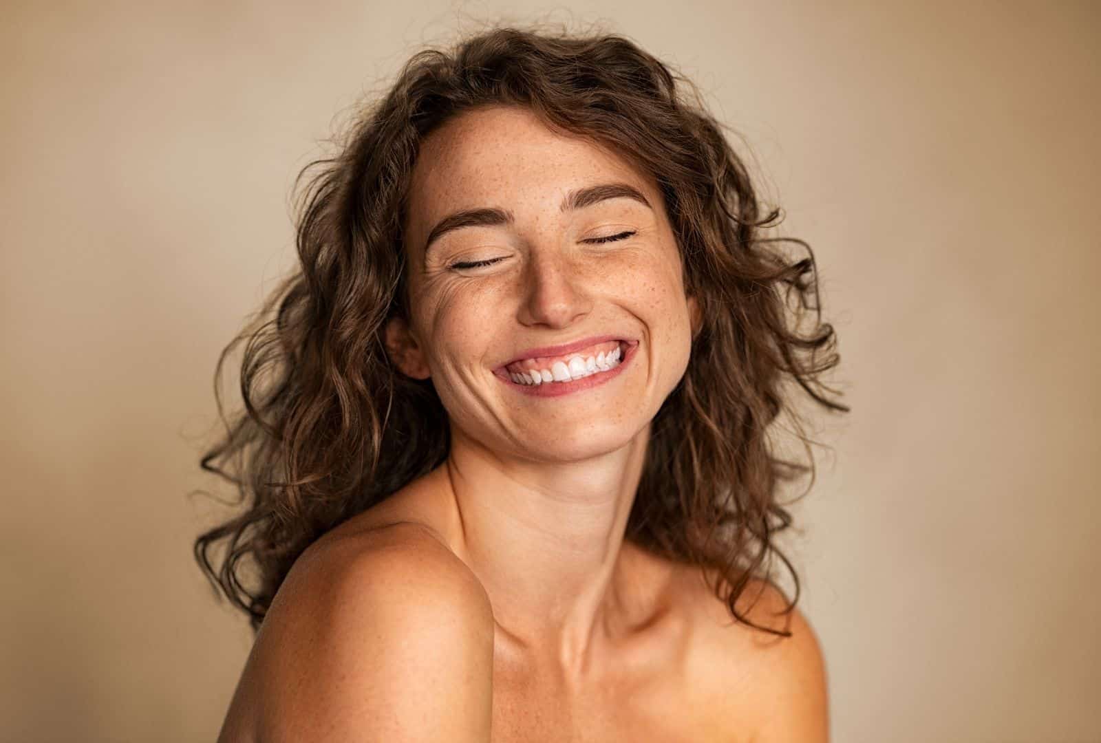 אישה מחייכת ומשוחררת, מסמלת פריצת דרך רגשית בטיפול בהתמכרויות – איך טראומות עבר בגמילה הופכות לכוח החלמה. תמונה מעוררת תקווה למי שמחפש גמילה רגשית.