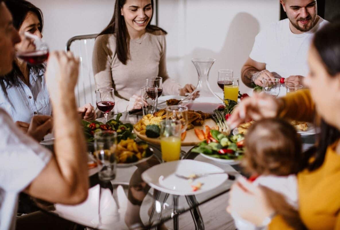 משפחה ישראלית רב-דורית יושבת סביב שולחן עמוס אוכל טרי, צוחקת ומשתפת ארוחה חמה יחד, מסמלת חזרה לקשרים והחלמה.